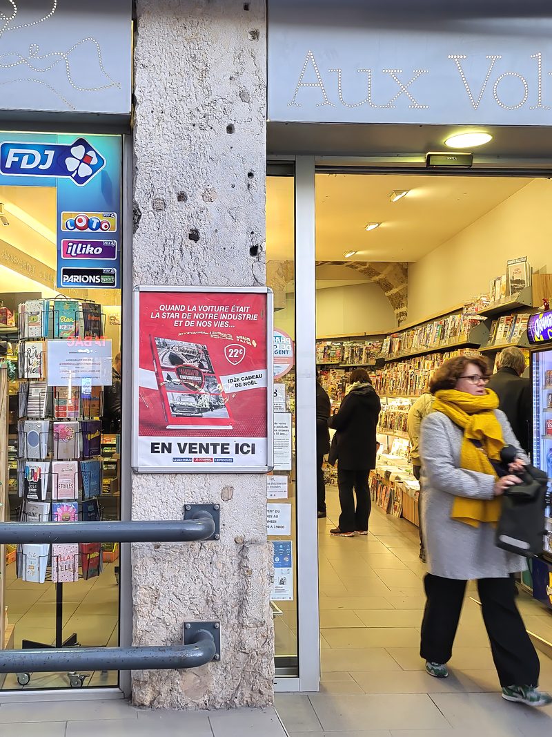 Affiche sur pilier dans une galerie commerciale, une passante devant la boutique