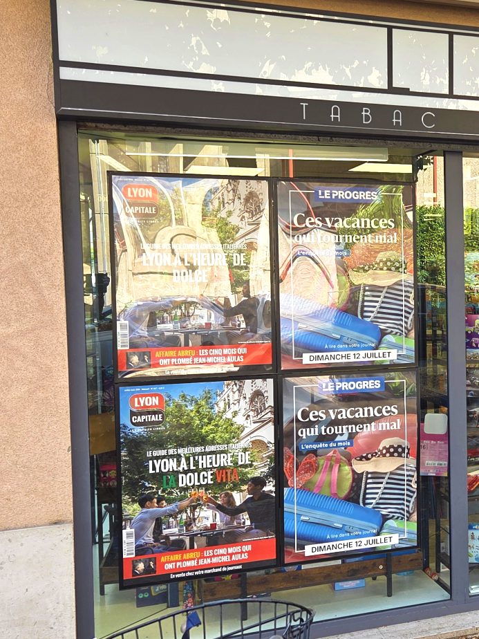 Devanture de librairie tabac-presse avec quatre affiches encadrées en vitrine