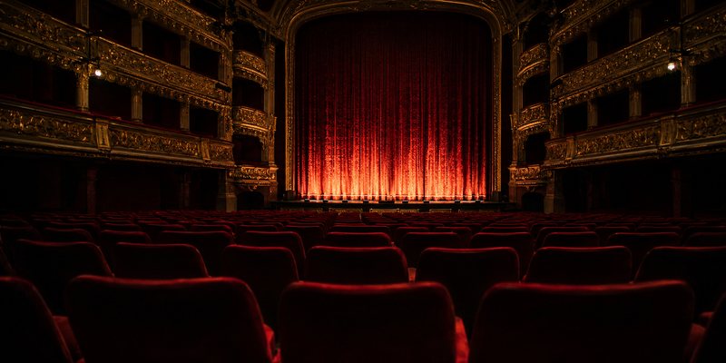 Salle de théâtre à l'italienne, rideau rouge éclairé avant le lever de rideau